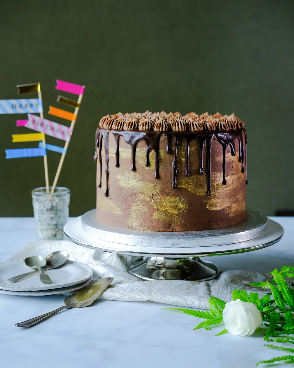 A chocolate celebration cake with gold detailing on a cake stand